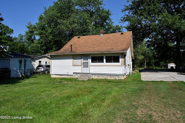 back of property with entry steps, a yard, and a shingled roof