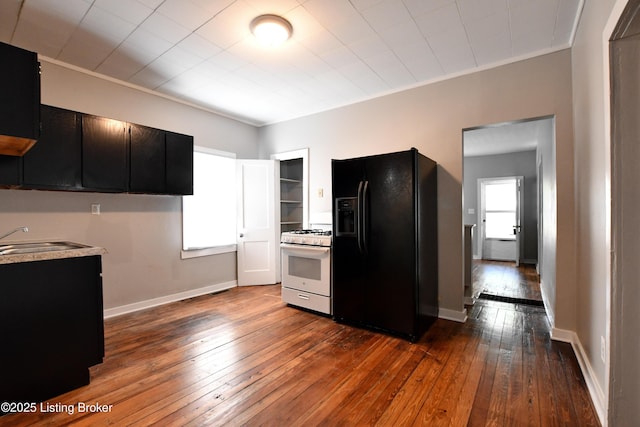 kitchen featuring dark cabinets, dark wood-type flooring, black fridge, white gas stove, and a sink