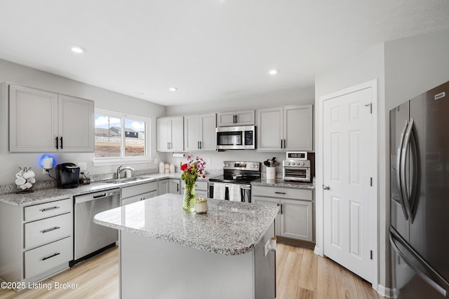 kitchen with light stone countertops, light wood finished floors, a kitchen island, and appliances with stainless steel finishes