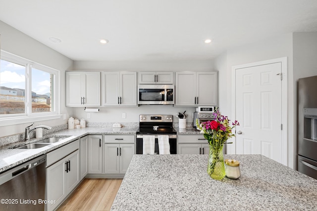 kitchen featuring stainless steel appliances, recessed lighting, light wood-style flooring, a sink, and light stone countertops