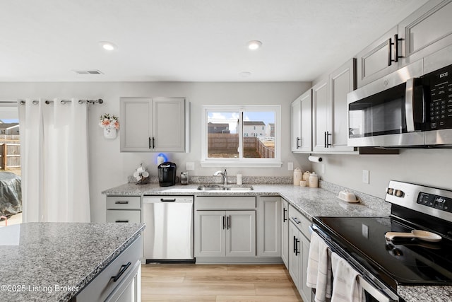 kitchen with stainless steel appliances, a sink, visible vents, light wood-style floors, and light stone countertops