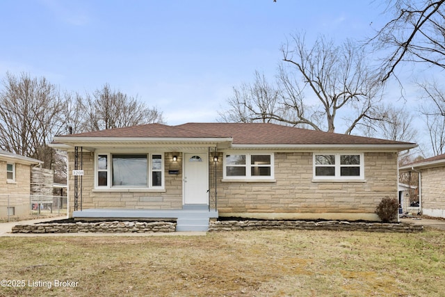 view of front facade featuring a front yard, stone siding, roof with shingles, and fence