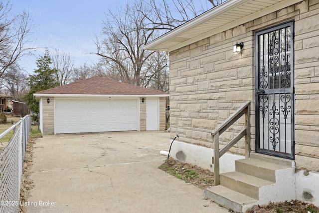 exterior space featuring stone siding, roof with shingles, a detached garage, and fence