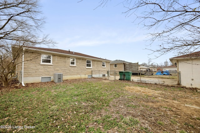 back of property featuring central AC unit, stone siding, fence, and a lawn