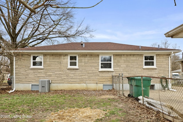 view of home's exterior with stone siding, fence, cooling unit, and roof with shingles