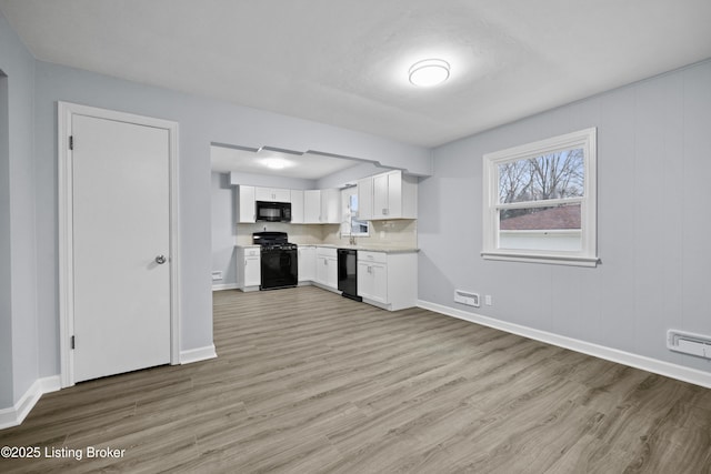 kitchen with light countertops, light wood-style flooring, white cabinetry, black appliances, and baseboards