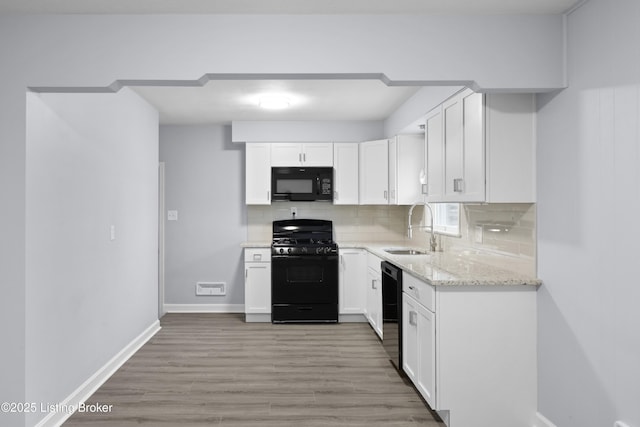 kitchen with light stone counters, a sink, black appliances, white cabinetry, and backsplash