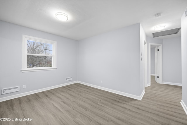 spare room featuring attic access, visible vents, baseboards, and wood finished floors