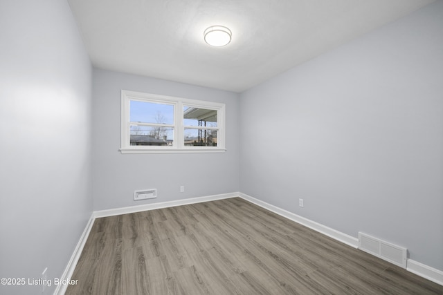 empty room with baseboards, visible vents, and wood finished floors