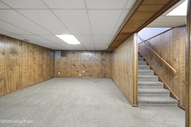 finished basement with stairway, a drop ceiling, light colored carpet, and wooden walls