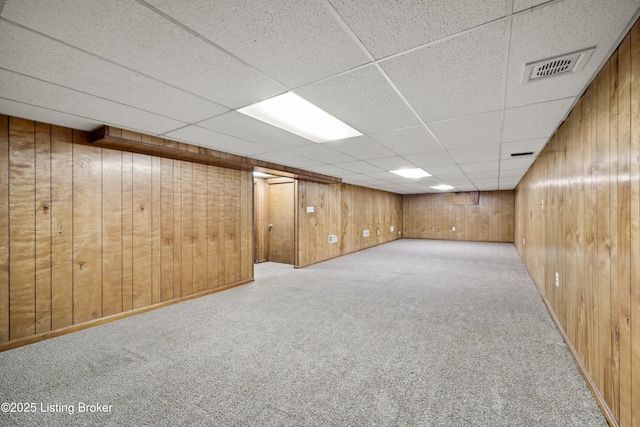 finished below grade area with a paneled ceiling, wood walls, carpet, and visible vents