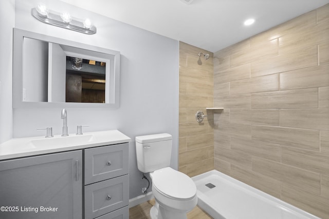 bathroom with tiled shower, vanity, toilet, and baseboards