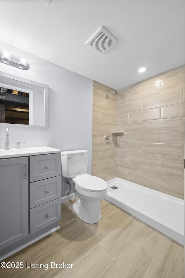 bathroom featuring visible vents, toilet, vanity, tiled shower, and baseboards