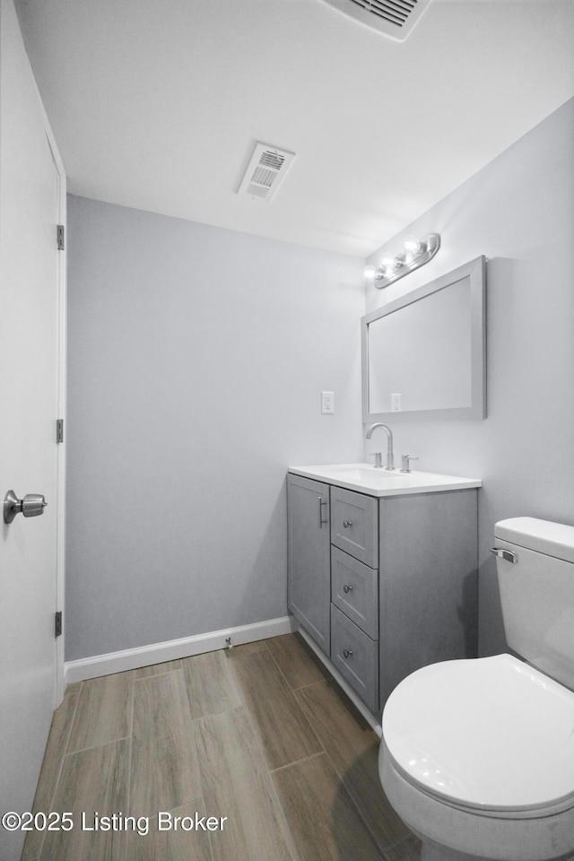 bathroom with baseboards, visible vents, toilet, wood finished floors, and vanity