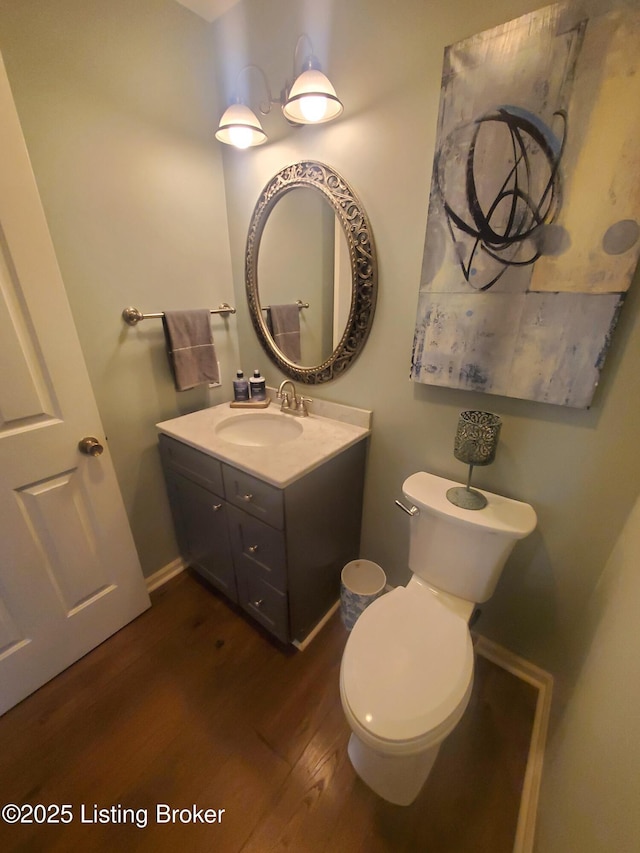 half bathroom featuring toilet, wood finished floors, vanity, and baseboards