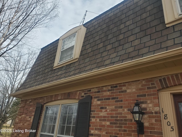 view of side of property featuring brick siding, roof with shingles, and mansard roof