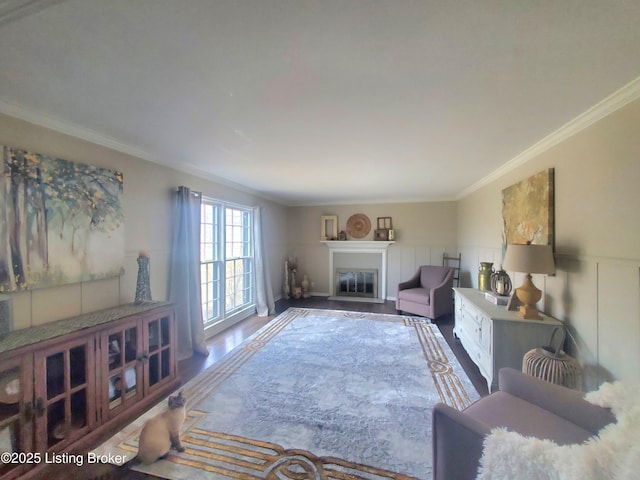 living room with wainscoting, a glass covered fireplace, ornamental molding, wood finished floors, and a decorative wall