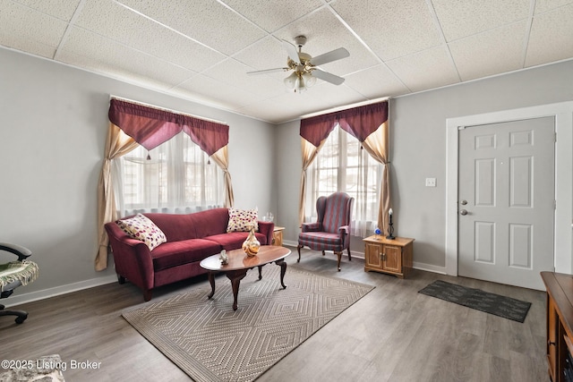 living area with a paneled ceiling, ceiling fan, baseboards, and wood finished floors