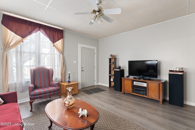 living room featuring light wood-type flooring, a ceiling fan, baseboards, and a drop ceiling