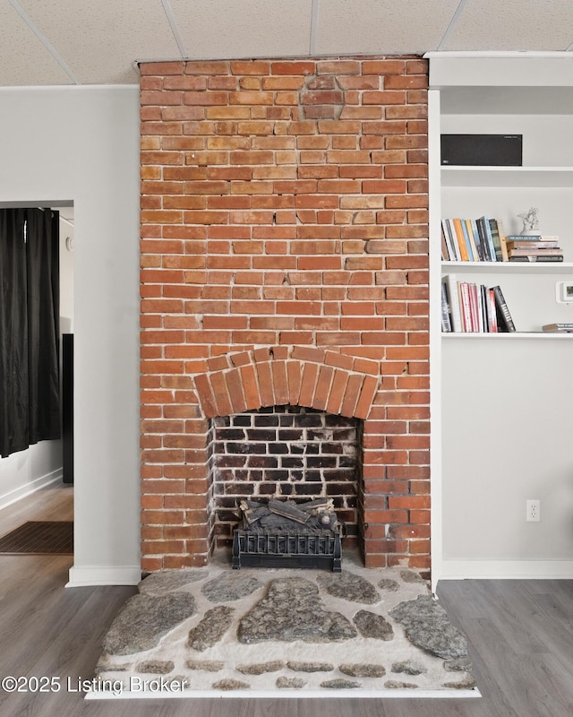 interior details featuring a drop ceiling, a fireplace, wood finished floors, and baseboards