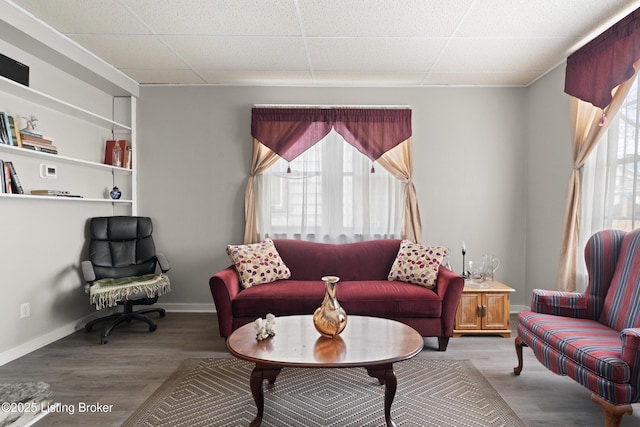 living room featuring a paneled ceiling, baseboards, and wood finished floors