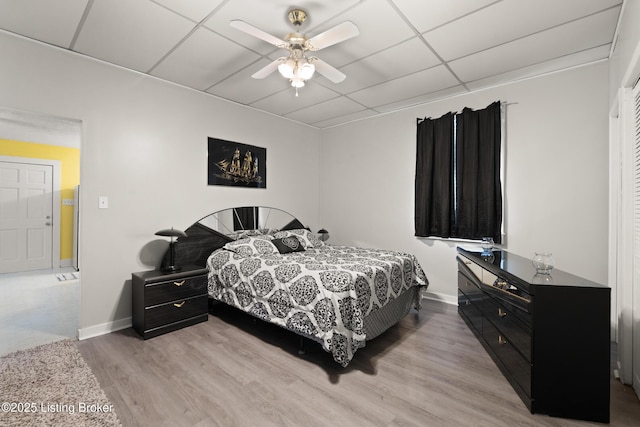 bedroom featuring light wood finished floors, ceiling fan, baseboards, and a drop ceiling