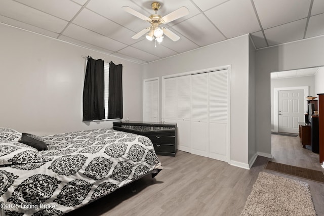 bedroom featuring a paneled ceiling, a closet, ceiling fan, light wood-type flooring, and baseboards