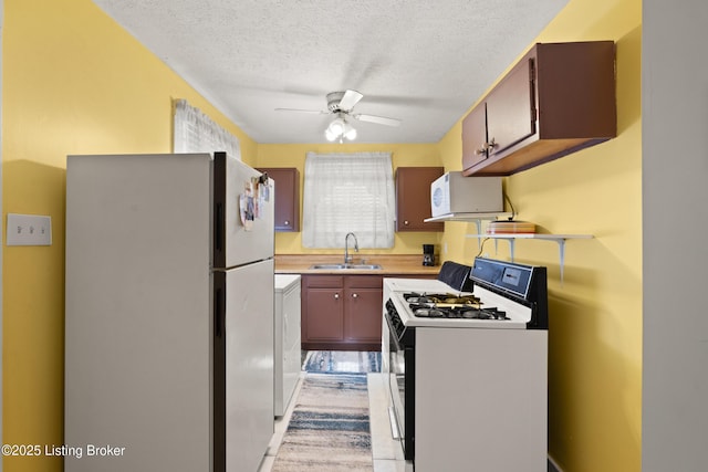 kitchen with white appliances, a sink, a ceiling fan, light countertops, and washer / dryer