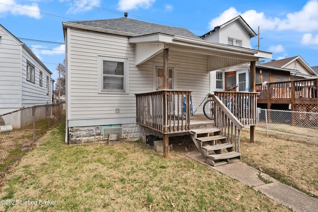 rear view of property featuring a deck, roof with shingles, a lawn, and a fenced backyard