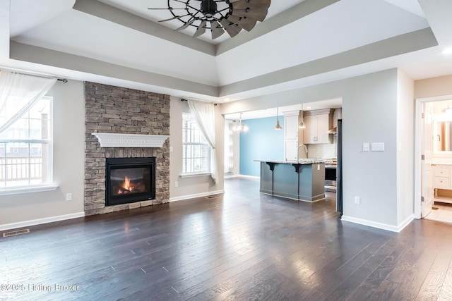 unfurnished living room featuring plenty of natural light, visible vents, a raised ceiling, and dark wood finished floors