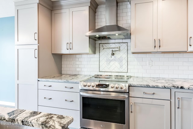 kitchen with electric range, wall chimney range hood, backsplash, and light stone counters