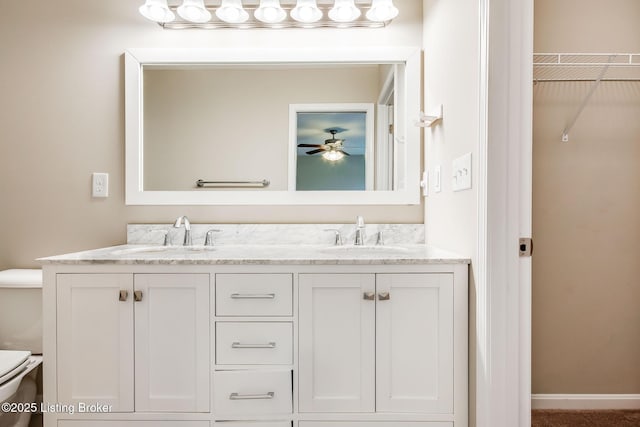 bathroom with toilet, double vanity, baseboards, and a sink