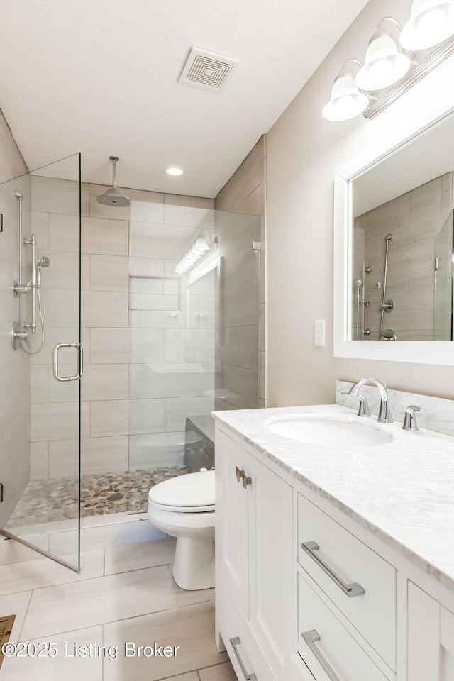 bathroom with toilet, a shower stall, visible vents, and vanity