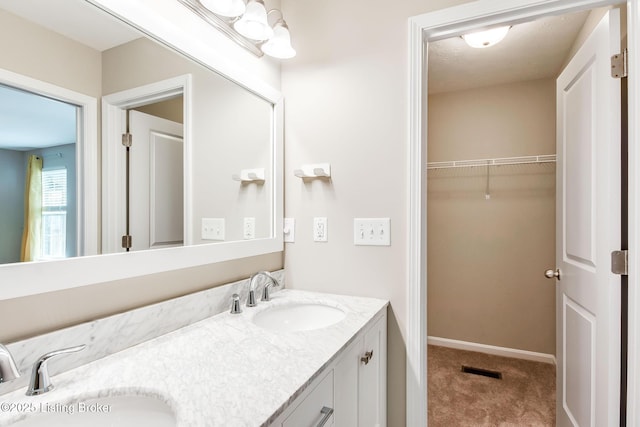 bathroom with a spacious closet, double vanity, a sink, and baseboards