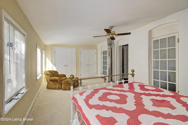 carpeted bedroom with a ceiling fan, brick wall, baseboards, and two closets