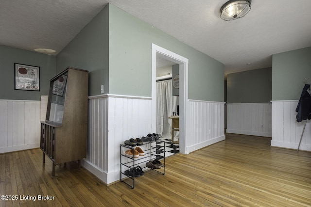 hall featuring wood-type flooring, wainscoting, and a textured ceiling