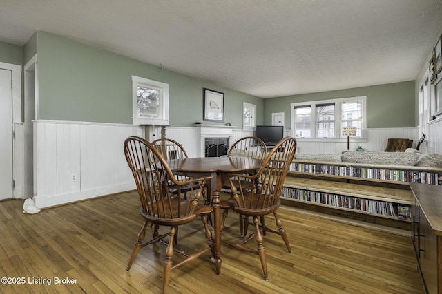 dining room featuring a textured ceiling, a fireplace, hardwood / wood-style floors, and wainscoting