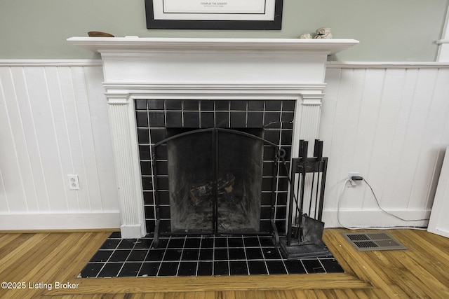 interior details with wainscoting, a tiled fireplace, wood finished floors, and visible vents