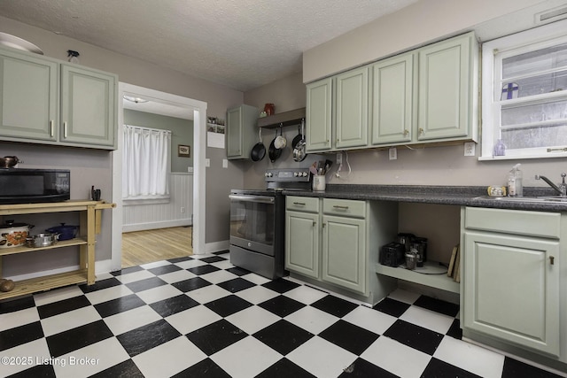 kitchen featuring black microwave, a wainscoted wall, a sink, stainless steel range with electric cooktop, and light floors