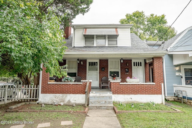 bungalow featuring a shingled roof, covered porch, brick siding, and fence