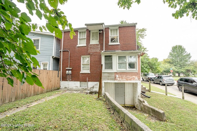 rear view of house with a yard, brick siding, and fence