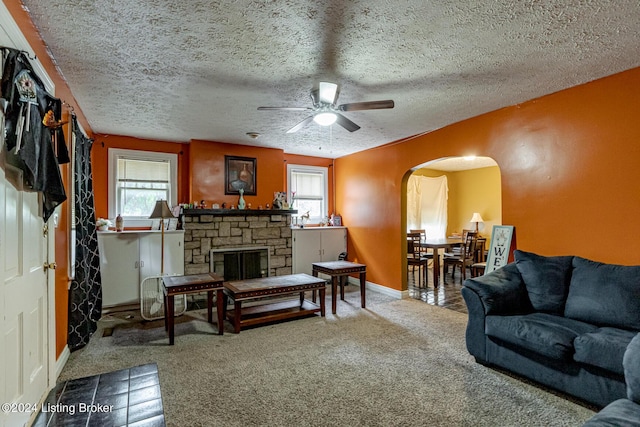 living area featuring arched walkways, a textured ceiling, a fireplace, carpet flooring, and baseboards