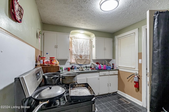 kitchen with a textured ceiling, white cabinetry, and a sink