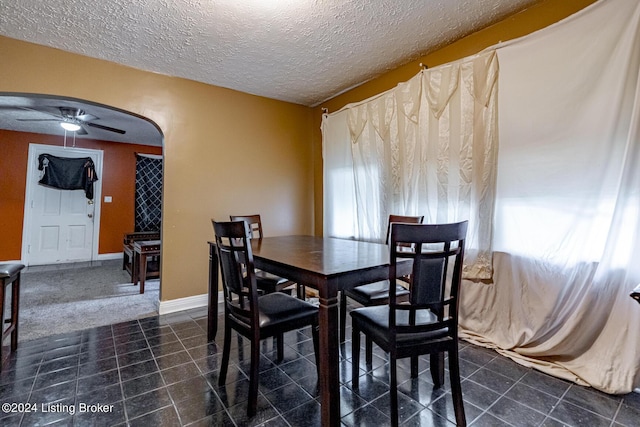 dining space featuring arched walkways, ceiling fan, a textured ceiling, dark tile patterned floors, and baseboards