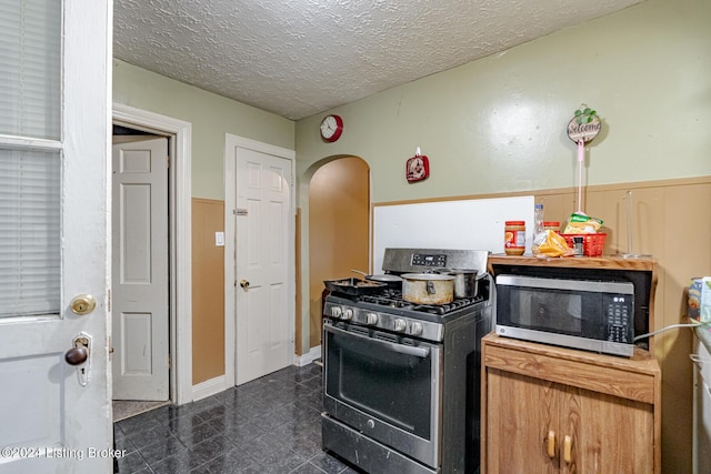 kitchen featuring arched walkways, granite finish floor, appliances with stainless steel finishes, a textured ceiling, and baseboards