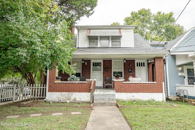 bungalow-style house featuring covered porch, a shingled roof, fence, and brick siding