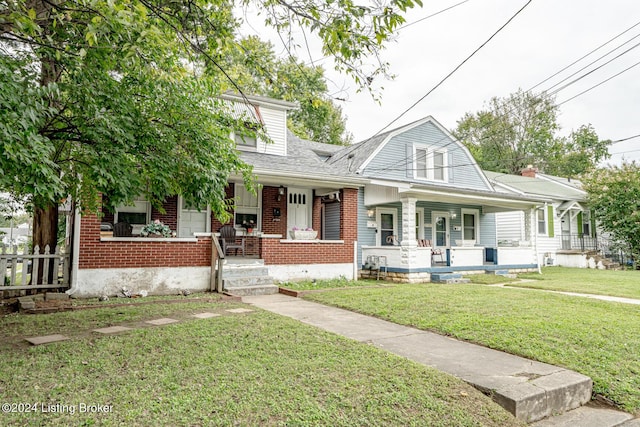 view of front of house with a porch, roof with shingles, a front yard, and brick siding