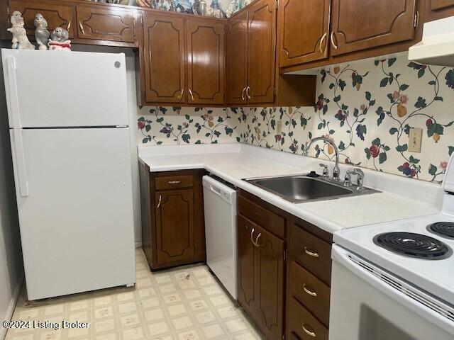 kitchen with white appliances, a sink, light floors, and wallpapered walls