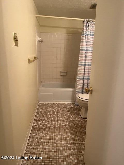 bathroom with a textured ceiling, toilet, shower / tub combo, visible vents, and baseboards