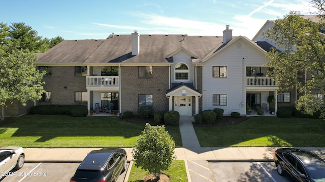 view of front facade featuring brick siding, a chimney, a front yard, and uncovered parking